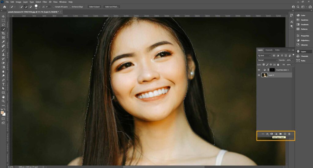 A woman smiling while using Adobe Photoshop, focused on creating a layer mask for hair adjustments.