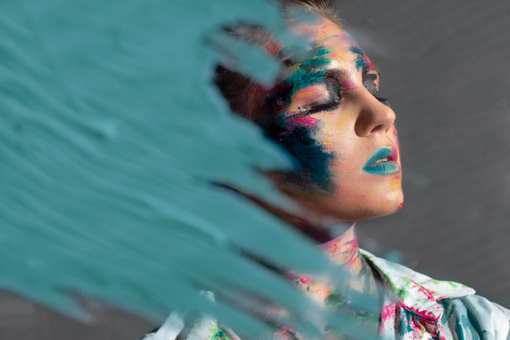Artistic headshot of a woman adorned with face paint and blue body paint, highlighting her creative expression.