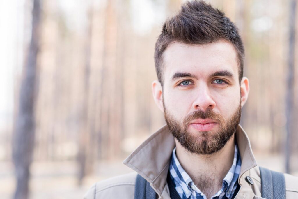 A bearded man wearing a backpack, with a blurred headshot background