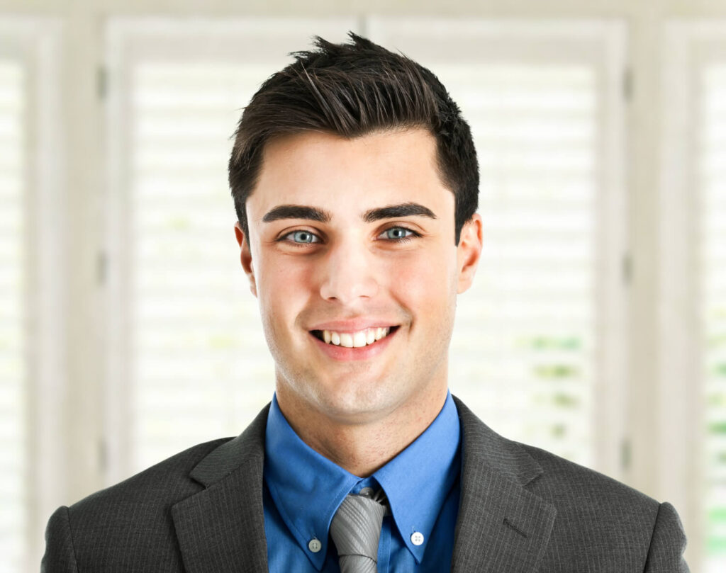 A smiling man in a suit and tie poses for a professional business headshot.