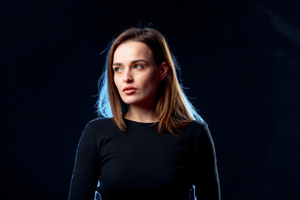 Headshot of a woman in a black shirt, standing confidently in front of a dark, dramatic background.