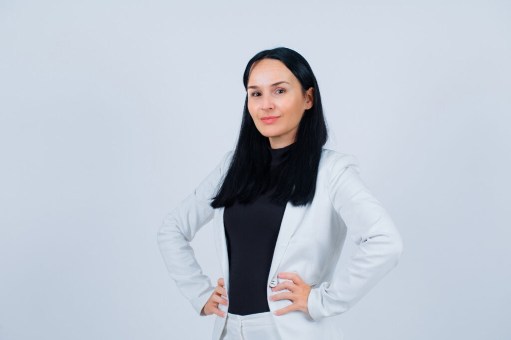 A woman in a white suit poses for the camera against a gray background in a professional headshot.