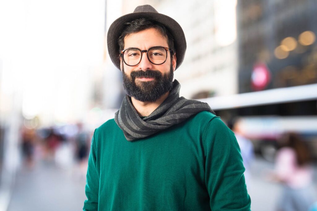 A bearded man wearing glasses stands confidently in an urban setting, suitable for a social media headshot.