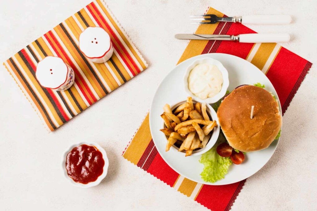 A top-down food photograph showcasing a plate with a hamburger, a serving of fries, and a dish of ketchup.