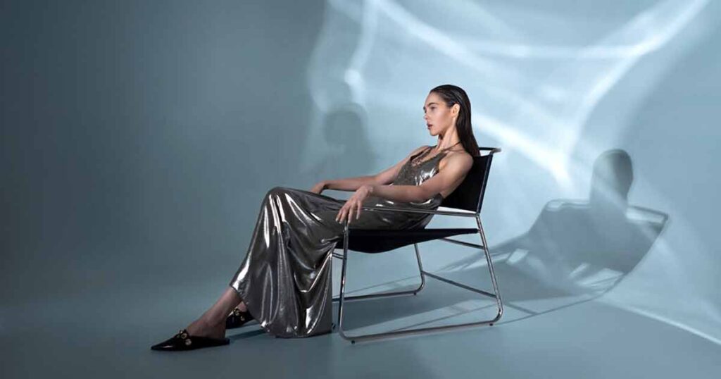 A woman in a silver dress elegantly seated on a chair, showcasing high-end retouching in the image.